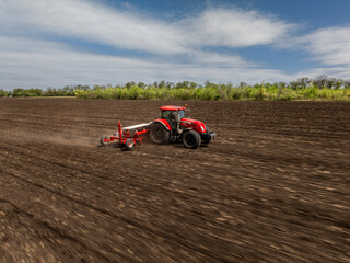 Obraz premium aerial view of a moving red tractor with seeder in ploughed field with motion blur