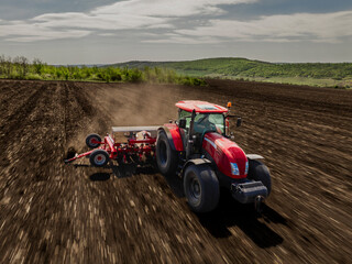 aerial view of a moving red tractor with seeder in ploughed field with motion blur
