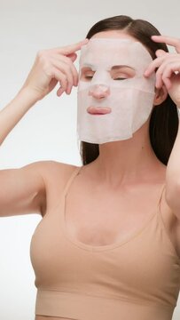 Beautiful brunette woman with clean skin applies a fabric face mask. Daily beauty routine