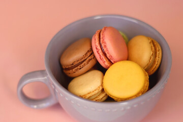 Purple cup filled with pastel macarons on pink background. Selective focus.