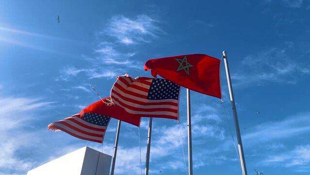 low angle view of morocco and USA flags waving with winds against blue sky