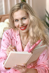 Beautiful blonde woman in pajamas writes in her diary in bed