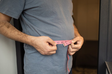 Overweight man measures his waist with measuring tape. Fat belly visceral fat. Body mass index,...