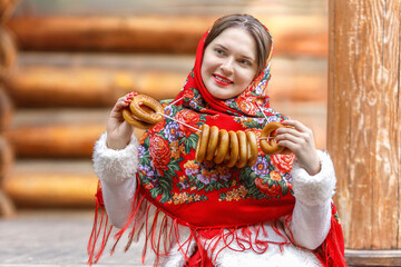 A beautiful Russian girl in red traditional Russian clothes holds bagels in her hands in the spring...