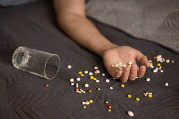 Selective focus, hand man miscellaneous colorful handful pills glass drug overdose, lying bed, committed suicide. Anxiety, depression, problems work and in the family, prevention, committing suicide