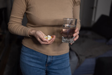 Young woman holding palm pills glass of water, preparing to take supplements or painkiller,...