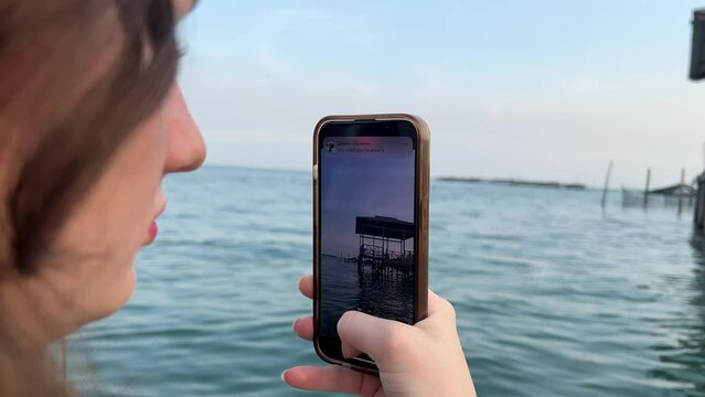 Girl takes a picture of a house on water on mobile phone