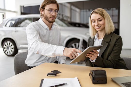Businessman choosing auto, buying new automobile in car showroom salon dealership store motor show. Caucasian rich man customer buyer client in suit sign contract on tablet with confident saleswoman.
