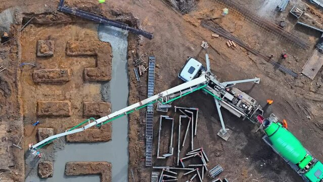 Time laps: Aerial view of rapid foundation pouring at a construction site, with a cement truck and pump dispensing concrete into an excavation for a multi-family home build.