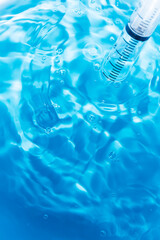 Syringe and blue water,Transparent drop of hyaluronic acid gel and a medical syringe for injections on a blue background. Top view, place for text.