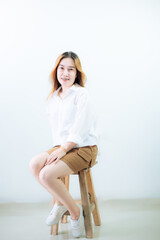 Young Asian woman sitting in a chair Isolated on white background. Studio cutout portrait of beautiful short-haired Asian female model in a long-sleeved white shirt and casual shoes, sitting cross-leg