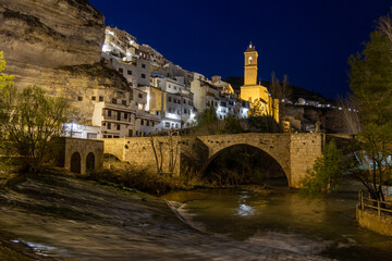 Alcalá del Júcar at night, located on a rock formed by the gorge of the Júcar River, cave houses roman bridge, castle, Church of San Andrés Apóstol (Albacete, Spain).