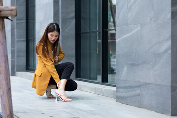 Health care injured foot ache - Asian business woman unhappy unwell sick ill and hold hand on leg ankle suffers pain. walking city urban street at business office center.