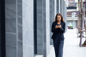 Fototapeta premium Mobile phone technology lifestyle - Hispanic business woman uses mobile phone device communicating with a colleague. Female walking outside modern office building