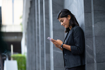 Mobile phone technology lifestyle - Portrait Smiling Young Businesswoman in black suit using smartphone at outside modern office building