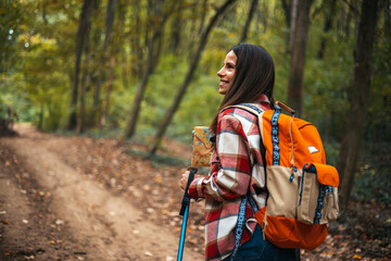 Back view portrait of young woman with backpack enjoying hiking in forest lit by sunlight, copy space. Beautiful Woman Hiker Smiling. Young woman hiking and going camping in nature - 786263662