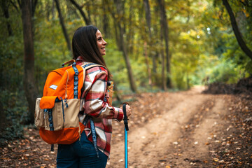 Back view portrait of young woman with backpack enjoying hiking in forest lit by sunlight, copy space. Beautiful Woman Hiker Smiling. Young woman hiking and going camping in nature - 786263819
