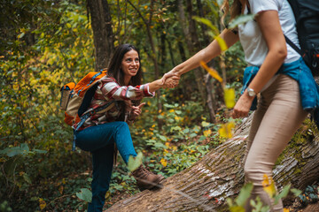 Happy women help while hiking up a rocky mountain in nature with backpack. Females friends exercise in nature park climbing and jumping while with sportswear training or trekking together outdoors - 786264257