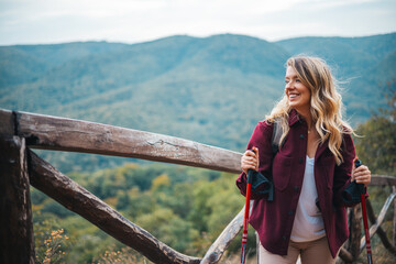 Portrait of a happy woman hiker standing on the slope of mountain ridge against mountains, blue cloudy sky on background. The woman is happy and looking at camera. Travel and active lifestyle concept. - 786265435
