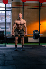 Fototapeta na wymiar in a sports club a bald trainer in sports shorts lifts weights on a barbell