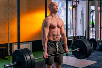 in a sports club a bald trainer in sports shorts lifts weights on a barbell
