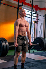 Fototapeta na wymiar in a sports club a bald trainer in sports shorts lifts weights on a barbell