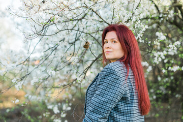 Beautiful red-haired woman enjoying smell in a flowering blooming spring garden. Spring blossom....