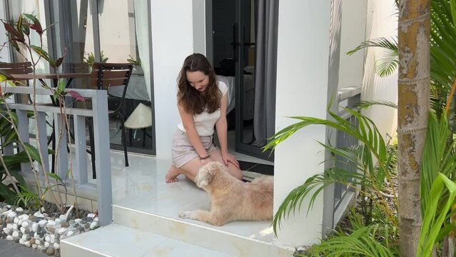 a girl stroking a dog's fur on the porch, a little housewife, a teenager and a fair old dog. hot country of palm trees