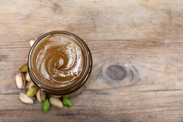 Tasty pistachio nut paste in jar on wooden table, top view. Space for text