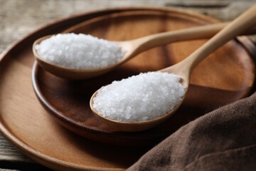 Organic salt in spoons on wooden table, closeup