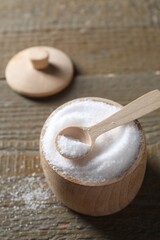 Organic salt in bowl and spoon on wooden table, closeup