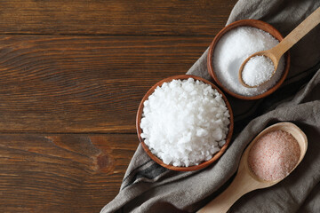 Different types of organic salt on wooden table, flat lay. Space for text