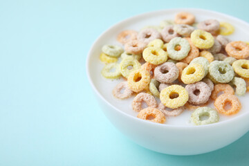 Tasty colorful cereal rings and milk in bowl on turquoise background, closeup. Space for text