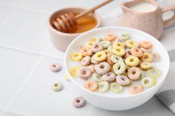 Cereal rings and milk in bowl on white tiled table, closeup. Space for text