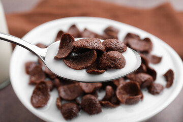 Breakfast cereal. Eating chocolate corn flakes and milk with spoon from bowl on table, closeup
