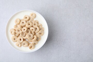 Breakfast cereal. Tasty corn rings with milk in bowl on grey table, top view and space for text