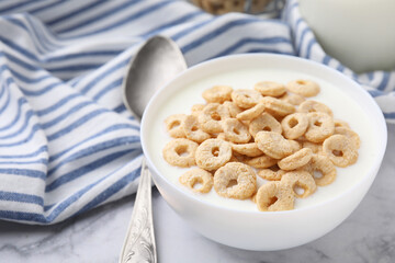 Breakfast cereal. Tasty corn rings with milk in bowl and spoon on white marble table, closeup