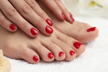 Obraz na płótnie Canvas Woman showing stylish toenails after pedicure procedure and manicured hands with red polish on white terry towel, closeup