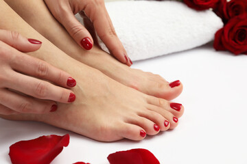 Woman with stylish red toenails after pedicure procedure and rose petals on white background,...