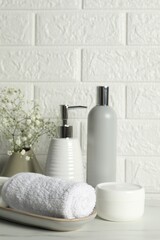 Different bath accessories, personal care products and gypsophila flowers in vase on white table near brick wall