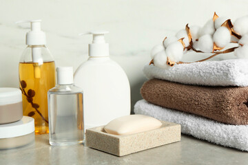 Bath accessories. Personal care products, terry towels and cotton flowers on gray table near white marble wall