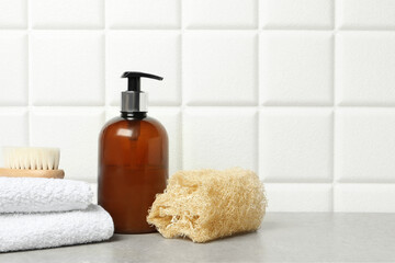 Different bath accessories and cosmetic bottle on gray table near white tiled wall, space for text