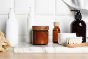 Different bath accessories and personal care products on wooden table near white tiled wall