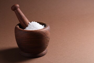 Natural salt in mortar and pestle on brown background. Space for text