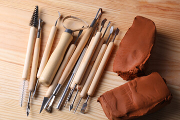 Clay and set of modeling tools on wooden table, flat lay
