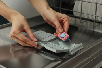 Woman putting detergent tablet into open dishwasher, closeup