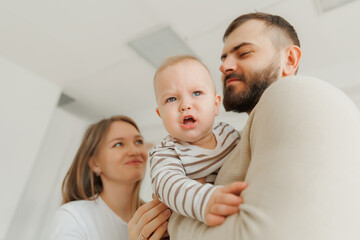 Naklejka premium Happy baby boy receives kisses from his loving parents, creating heartwarming scene during first birthday celebration at home. Lifestyle moment of scandinavian family