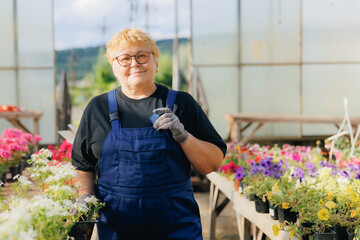 Concept flower seller in greenhouse, online shop. Portrait senior gardener woman working in garden farm plants