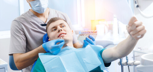 Young man smiling while looking at mirror in dental chair in clinic, top view, concept dentistry banner