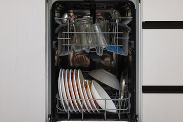 Open modern dishwasher with dirty tableware in kitchen